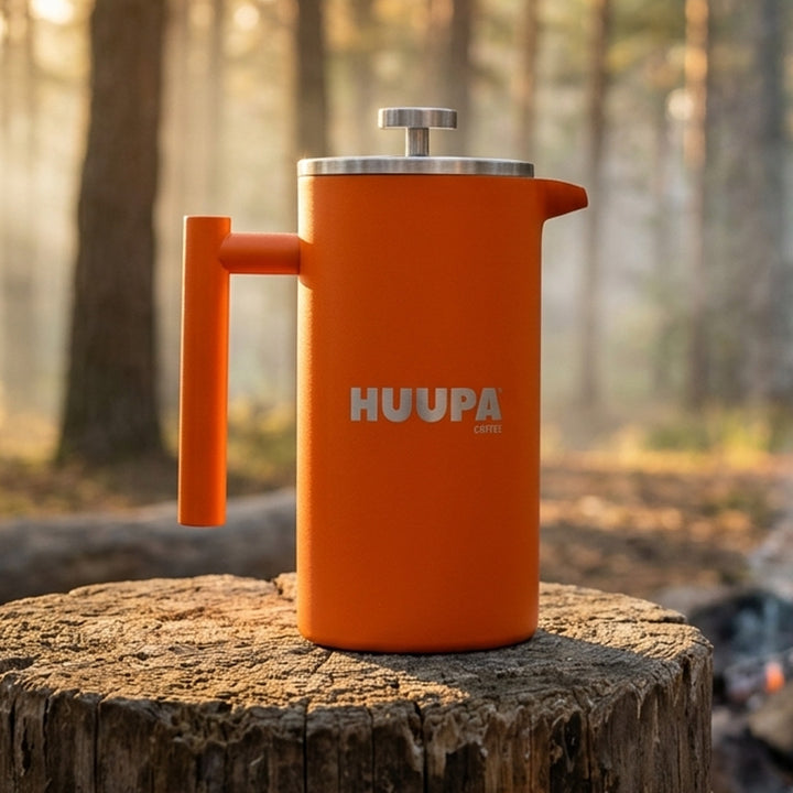 Prensa francesa naranja 1 L marca Huupa en tronco de madera en la naturaleza