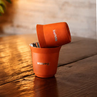 vaso medidor de espresso 80ml naranja marca HUUPA sobre mesa de madera