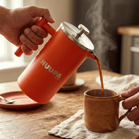 Prensa francesa naranja 1 L marca Huupa sirviendo taza de café en mesa de madera 